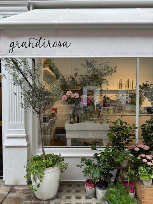 The image shows the exterior of 'grandirosa,' a floral shop with a large glass window displaying an interior filled with various floral arrangements and vases. Outside, there are several potted plants